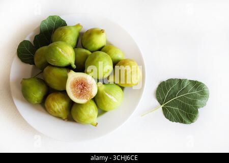 Fig fruit. A group of fresh green ripe figs in a white plate on a white table. Healthy and vegetarian food. Close-up. Directly above. Stock Photo