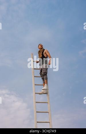 Man Standing on Tall Ladder Against Clear Blue Sky in Desert Stock Photo