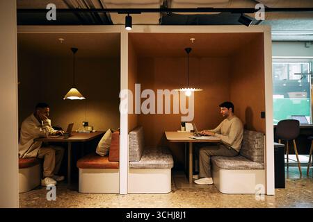 Multiracial businessmen working on laptop while sitting in illuminated coworking space at office Stock Photo