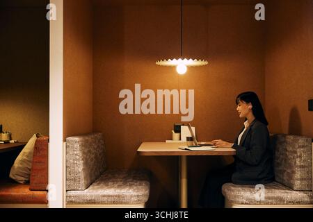 Side view of female business entrepreneur talking on video call through laptop while sitting on sofa at illuminated cowo Stock Photo