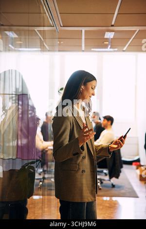 Female entrepreneur talking on video call through smart phone while standing near glass wall in office Stock Photo