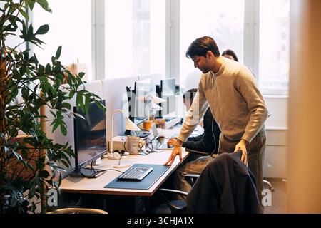 Young businessman going to sit on chair at desk with computer in office Stock Photo