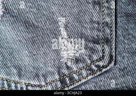 Gray denim fabric with visible yellow stitching and frayed threads creating textured background for modern casual fashion and clothing design Stock Photo