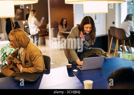 Female business professional talking on smart phone while using laptop on table in coworking office Stock Photo