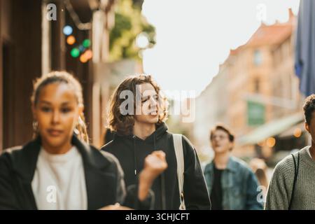 Young man spending leisure time with friends walking at street on sunny day Stock Photo