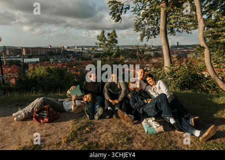 Group of young male and female friends spending leisure time sitting on hill Stock Photo
