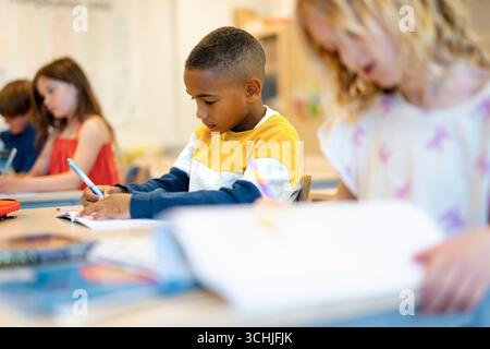 Schoolboy writing in book while sitting at desk in classroom Stock Photo