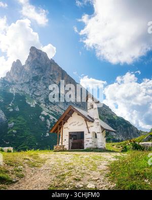 Small mountain chapel dedicated to Visitation at Falzarego Pass surrounded by towering Dolomites limestone cliffs under dramatic cloudy sky in summer Stock Photo