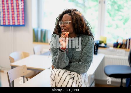 Smiling female teacher sitting on desk while teaching students in classroom Stock Photo