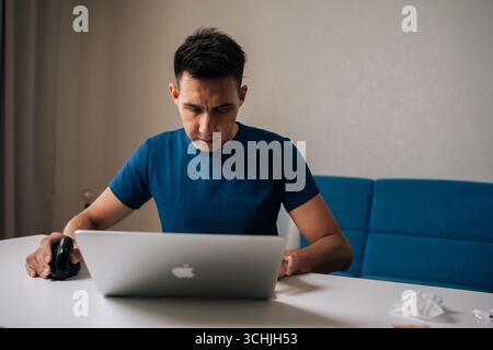 Portrait of successful freelancer male concentrating on work sitting at table in modern home office, using vertical mouse and laptop Stock Photo
