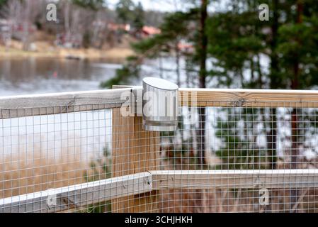 A sleek stainless steel solar-powered outdoor lamp is mounted on a wooden fence with wire mesh, providing eco-friendly lighting for gardens, patios, o Stock Photo