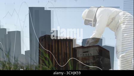 Leaning beekeeper in suit inspecting hives on grass, with skyline and graph overlays, copy space Stock Photo