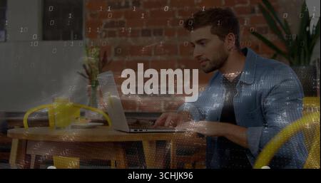Typing man in denim shirt working on laptop at wooden cafe table, with yellow headphones, plants Stock Photo