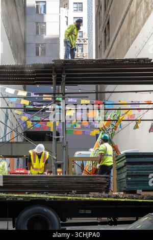 Workers dismantling a sidewalk bridge structure in Midtown Manhattan in front of bright decorative pennant strings, 2025, New York City, United States Stock Photo