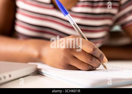 Close up of african american woman hand jotting down marketing ideas on notepad while working remotely. Black female employee writing on paper to organize business tasks at home office desk. Stock Photo