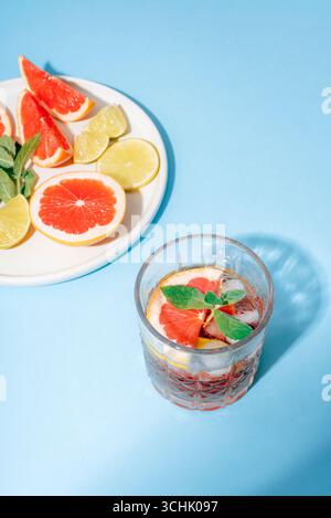 Refreshing cocktail with grapefruit, lime and mint in glass with ice. Citrus drink on blue background with shadows. Top view. Stock Photo