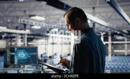 Jolly IT professional monitors server room activity using tablet in facility. Happy data center technician reviews rigs tests results with device to ensure systems are working correctly, camera B Stock Photo