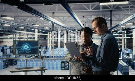 Team of engineers in server hub optimizing deep learning AI systems handling tasks. Teamworking data center colleagues adjust artificial intelligence model parameters using device, camera A Stock Photo
