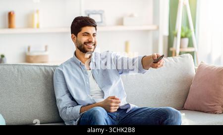 Watching TV. Happy arab man having rest, switching channels with remote controller Stock Photo