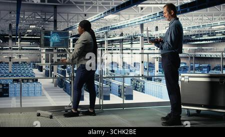 Data center software developers monitor deep learning processes, reviewing operational metrics. Server farm IT specialists work together to review neural networks reports during inspection, camera A Stock Photo