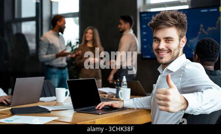 Confident businessman sitting at desk showing thumbs up gesture Stock Photo