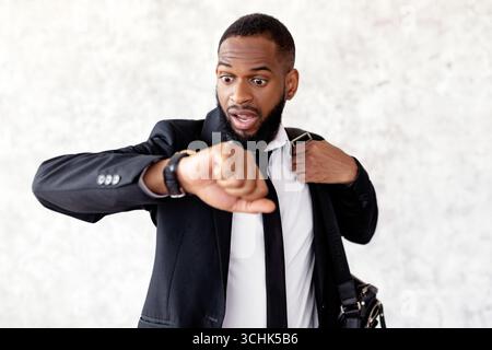Scared black man is late for work looking at watch Stock Photo