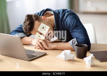 Exhausted arab guy with eyes drawing sleeping at workdesk Stock Photo