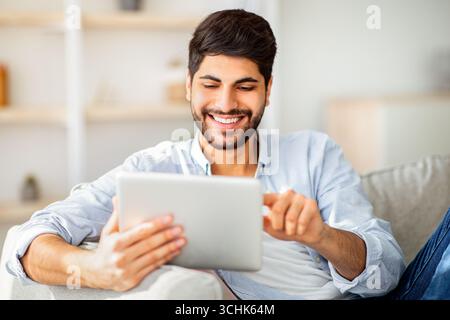 Happy arab man using digital tablet, shopping online, browsing internet or working remotely on tab computer Stock Photo