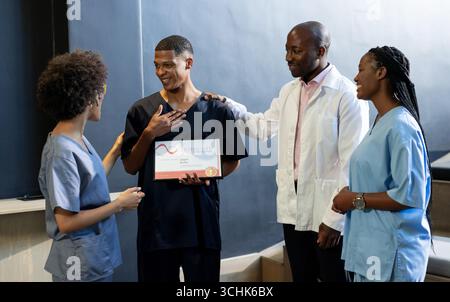 Celebrating colleague's achievement, medical diverse team in hospital hallway, at conference hall Stock Photo
