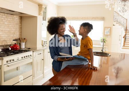 Mother and son sharing high five in kitchen, enjoying quality time together Stock Photo