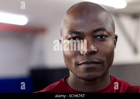African american man with shaved head in red shirt standing in gym under fluorescent lighting Stock Photo