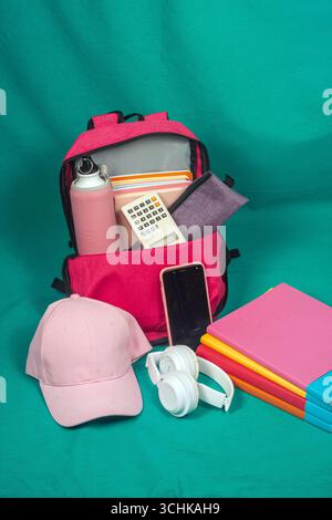 Pink backpack overflowing with school supplies on turquoise background Stock Photo