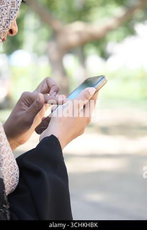 Muslim woman using smartphone outdoors in sunny park Stock Photo