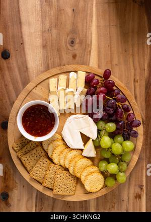 Cheese platter with grapes, crackers, and dip on wooden table, ready for celebration, at home Stock Photo