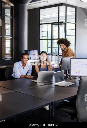 Diverse team collaborating on laptops in modern office, discussing digital analytics Stock Photo