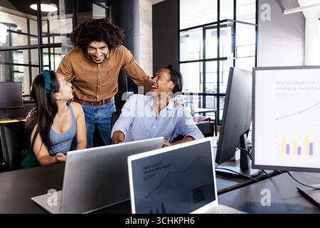 Diverse business team collaborating and laughing in modern office with laptops Stock Photo