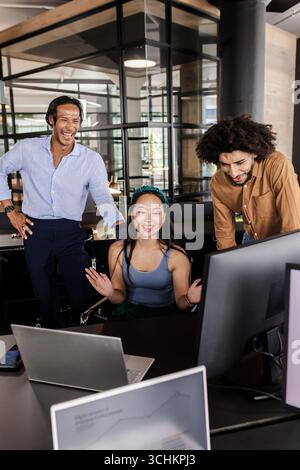 Diverse team collaborating enthusiastically around computer screens in modern office Stock Photo