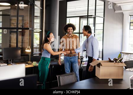 Diverse colleagues greeting each other in modern office, smiling and shaking hands Stock Photo