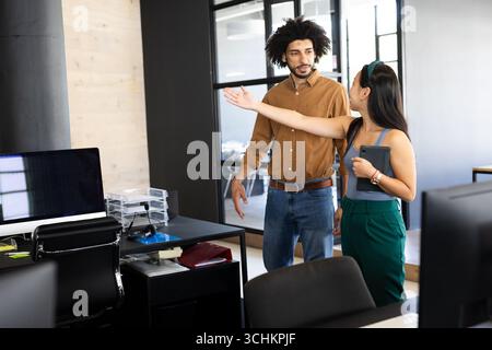 Diverse colleagues discussing project details in modern office, holding tablet and gesturing Stock Photo