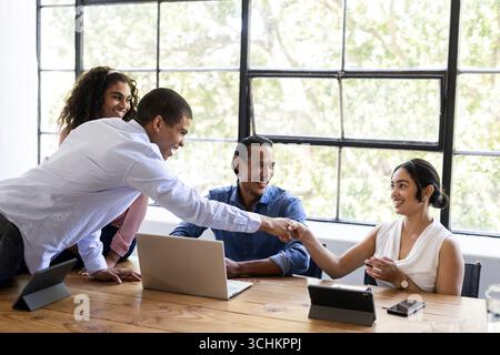 Diverse business team collaborating at office, shaking hands and smiling Stock Photo