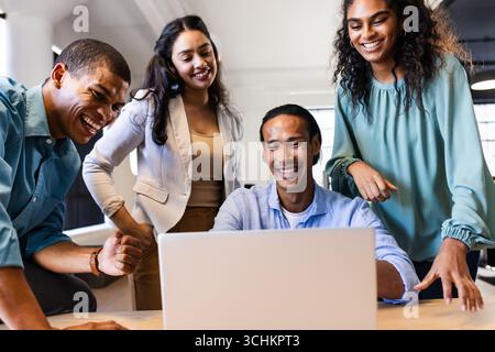 Diverse business team collaborating on laptop, smiling and discussing project ideas, at office Stock Photo