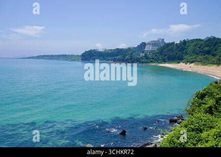 Hotels on the headland overlook Jungmun Saekdal Beach and turquoise water along Jeju’s south coast, seen from across the bay. Stock Photo