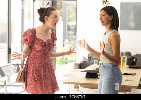 Two young women having lively conversation in sunlit dining room Stock Photo