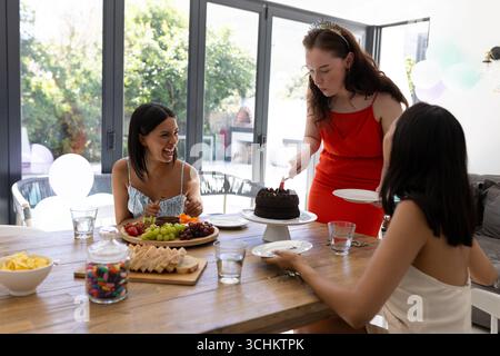 Cutting chocolate cake, young women celebrate at home with laughter and joy Stock Photo