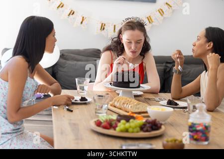 Celebrating birthday, three young women enjoy chocolate cake at wooden table Stock Photo
