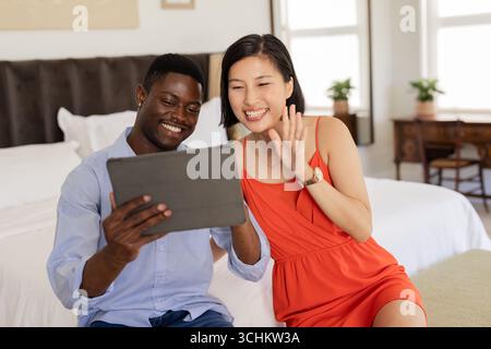 Smiling couple using tablet for video call in cozy bedroom setting Stock Photo