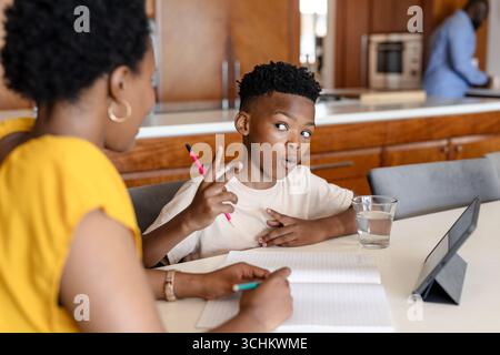 Mother and son studying together at kitchen table, using tablet and notebook Stock Photo