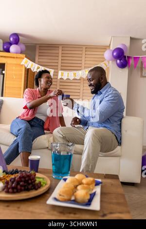 Celebrating at home, joyful couple toasting with drinks on cozy sofa Stock Photo