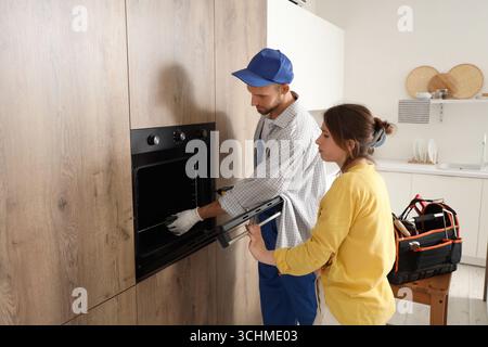 Young woman with male technician repairing electric oven in kitchen Stock Photo