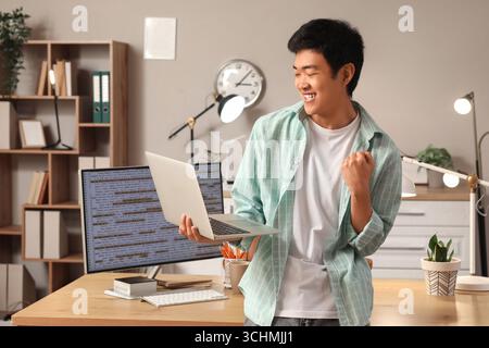 Happy male Asian programmer with laptop in office Stock Photo